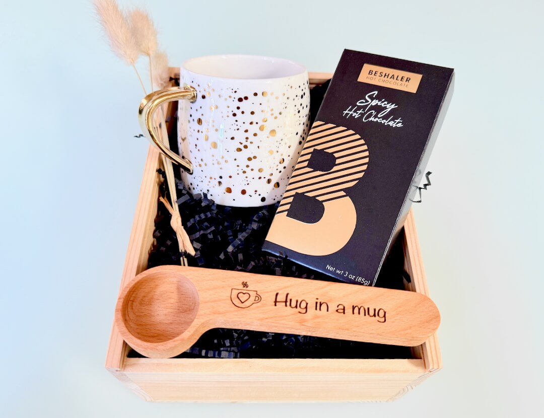 Gift set with mug, chocolate bar, and wooden spoon on a light blue background

